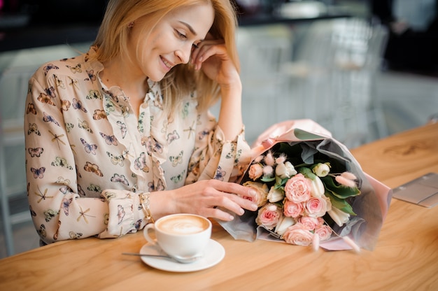 Jeune fille souriante assise à table avec une tasse de café et un beau bouquet