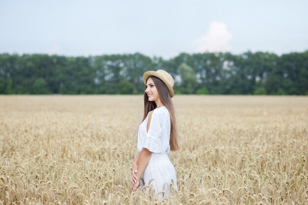 Jeune fille souriante au chapeau de paille est un batelier appréciant la nature du champ de blé.