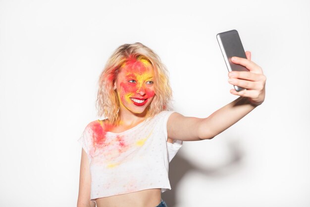 Jeune fille souriante aux couleurs Holi prenant selfie