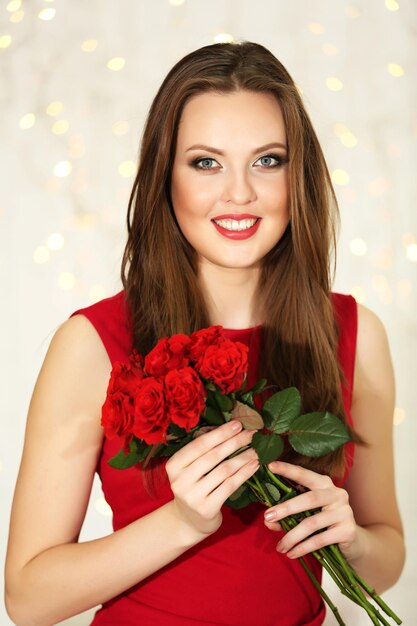 Jeune fille souriante avec bouquet de roses rouges sur fond de lumières