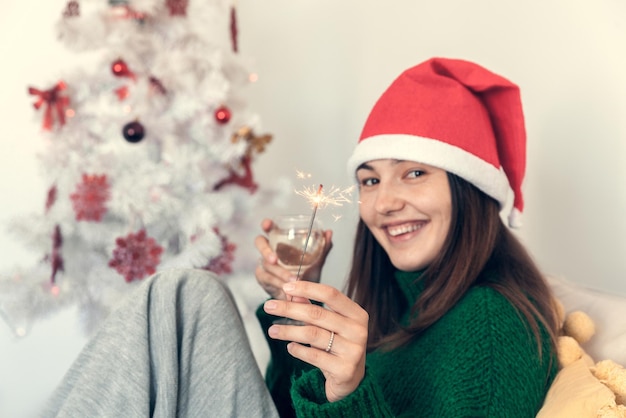 Jeune fille souriante avec une coupe de champagne et une lumière de Bengale portant un chapeau de père Noël