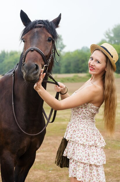 Jeune fille souriante dans un chapeau de paille et une robe d'été photographiée avec un cheval