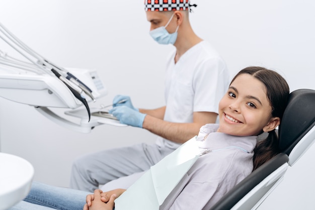 Jeune fille souriante dans un fauteuil dentaire. Le dentiste se prépare à travailler avec un jeune patient.