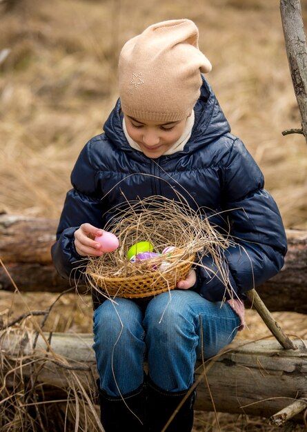 Jeune fille souriante dans la forêt regardant les oeufs de Pâques colorés dans le panier