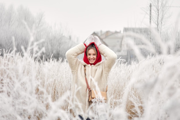 Une jeune fille souriante dans un manteau de fourrure blanche pose dans des buissons enneigés