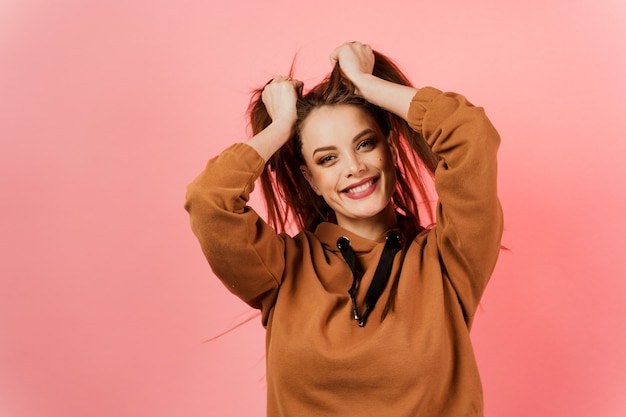 Jeune fille souriante dans un pull marron sur fond rose