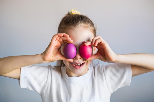 Jeune fille souriante dans un t-shirt blanc ferme les yeux avec des oeufs peints de Pâques multicolores Pâques Printemps