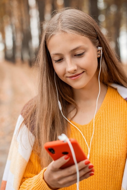 Jeune fille souriante écoutant de la musique dans un parc d'automne tout en se promenant