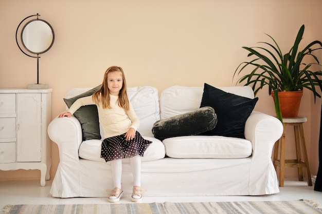 Jeune fille souriante est assise sur le canapé à la maison