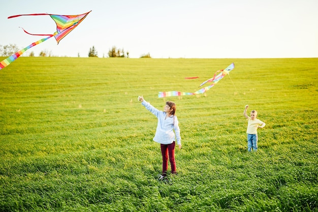 Jeune fille souriante et garçon frère courir avec des cerfs-volants colorés sur la prairie d'herbes hautes Moments d'enfance heureux