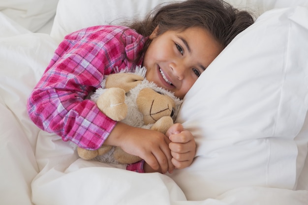 Jeune fille souriante avec un jouet en peluche au repos dans son lit