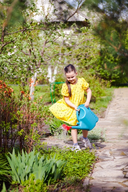 Une jeune fille souriante et joyeuse vêtue d'une robe jaune volant au vent arrose de jeunes fleurs d'un lac bleu...