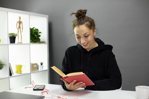 Jeune fille souriante, lisant un livre à la maison