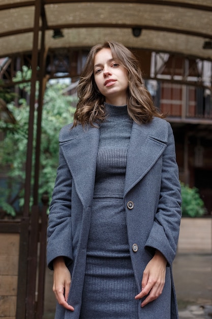 Jeune fille souriante en manteau gris et col roulé pose à l'extérieur