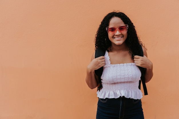 Jeune fille souriante portant un sac à dos en se tenant debout devant le mur