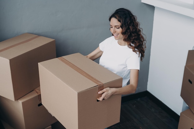 Jeune fille souriante propriétaire locataire tenant une boîte en carton emballée se déplaçant dans un nouvel appartement