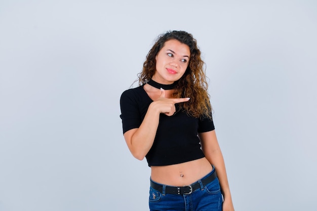 Jeune fille souriante regarde à droite en pointant vers la droite avec l'index sur fond blanc