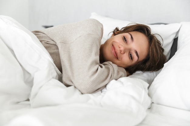 Une jeune fille souriante se détend au lit le matin.