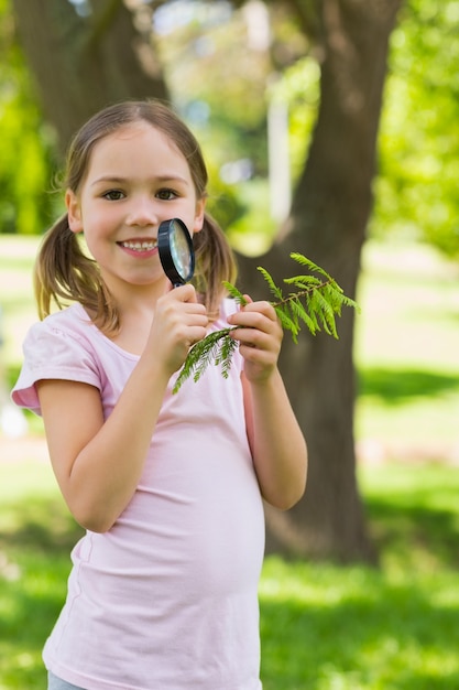 Jeune fille souriante tenant des feuilles et loupe au parc