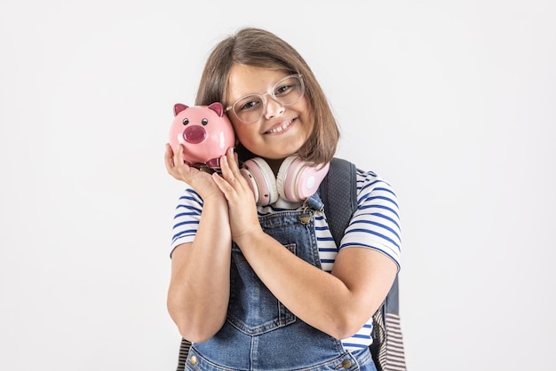 Une jeune fille sourit en tenant sa tête près d'une tirelire rose avec des économies