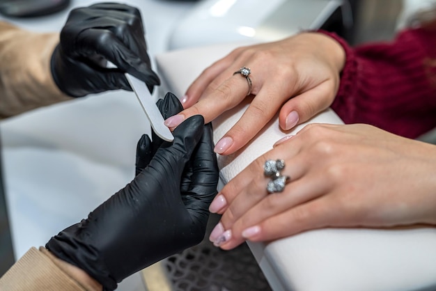 Une jeune fille spécialiste des ongles en mains avec une lime à ongles scie les ongles d'une cliente pendant l'épidémie. Notion d'ongle. Concept de manucure