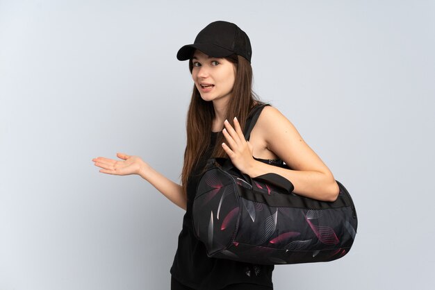 Jeune fille de sport avec sac de sport isolé sur gris avec expression de surprise tout en regardant côté