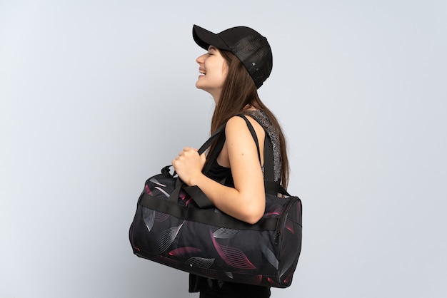 Photo jeune fille de sport avec sac de sport isolé sur gris rire en position latérale