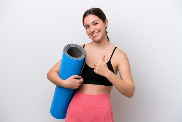 Jeune fille sportive allant à des cours de yoga tout en tenant un tapis isolé sur fond blanc en donnant un geste du pouce levé