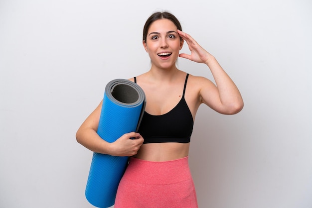 Jeune fille sportive allant à des cours de yoga tout en tenant un tapis isolé sur fond blanc avec une expression surprise