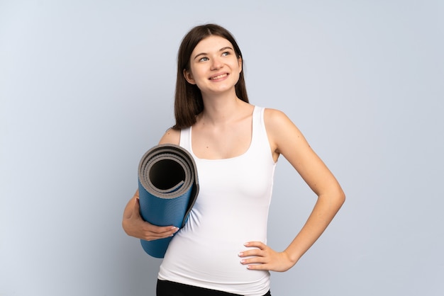 Jeune fille sportive allant à des cours de yoga tout en tenant un tapis posant avec les bras à la hanche et souriant