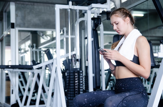 Jeune fille sportive au repos après une séance d&#39;entraînement intense dans une salle de sport avec un smartphone écoutant de la musique