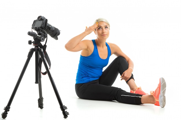 La jeune fille sportive aux cheveux blonds est assise devant la caméra, montre comment faire de l'exercice et elle est fatiguée