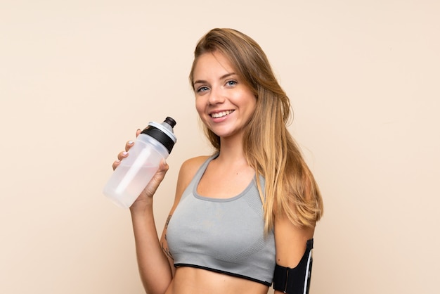 Jeune fille sportive blonde sur un mur isolé avec une bouteille d'eau de sport