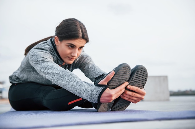 Jeune fille sportive faisant des exercices de yoga sur un tapis de fitness à l'extérieur près du lac pendant la journée