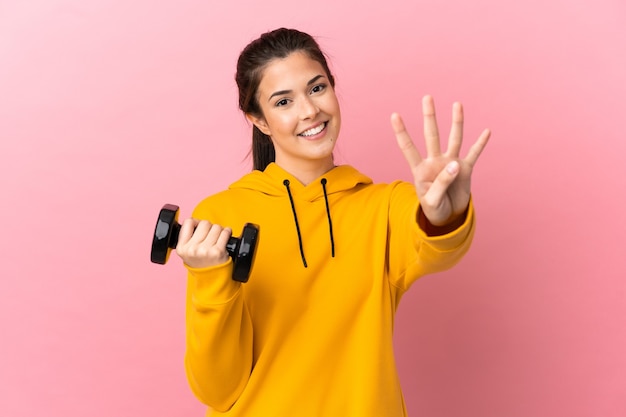 Jeune fille sportive faisant de l'haltérophilie sur fond rose isolé heureux et comptant quatre avec les doigts