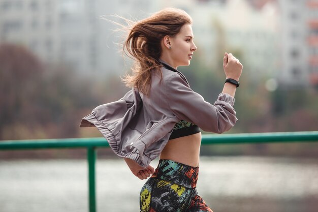 Jeune fille sportive jogging dans le parc de la ville au jour d'automne.