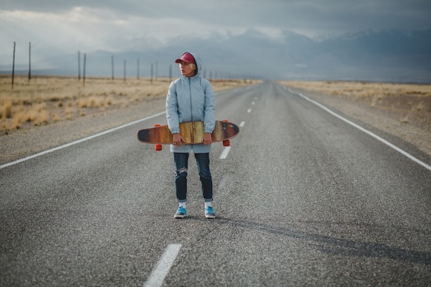 Jeune fille sportive avec longboard est debout sur une route déserte