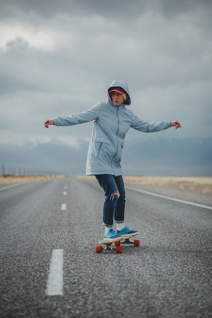 Jeune fille sportive avec longboard est debout sur une route déserte