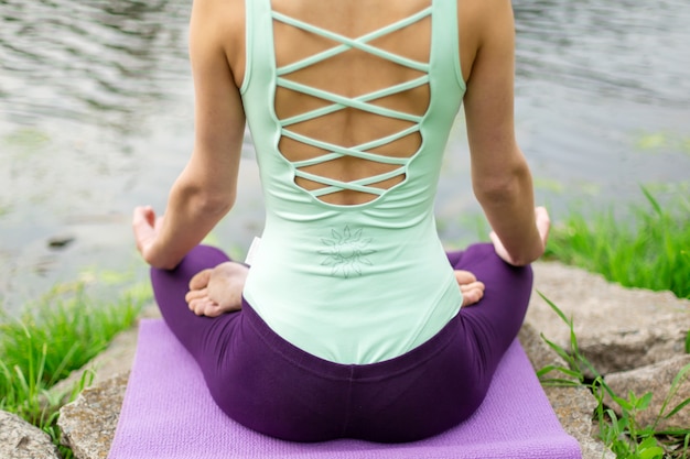 Une jeune fille sportive pratique le yoga sur une pelouse verte au bord de la rivière, la posture du yoga assans. Méditation et unité avec la nature