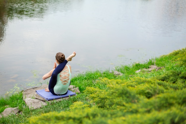 Une jeune fille sportive pratique le yoga sur une pelouse verte au bord de la rivière, la posture du yoga assans. Méditation et unité avec la nature