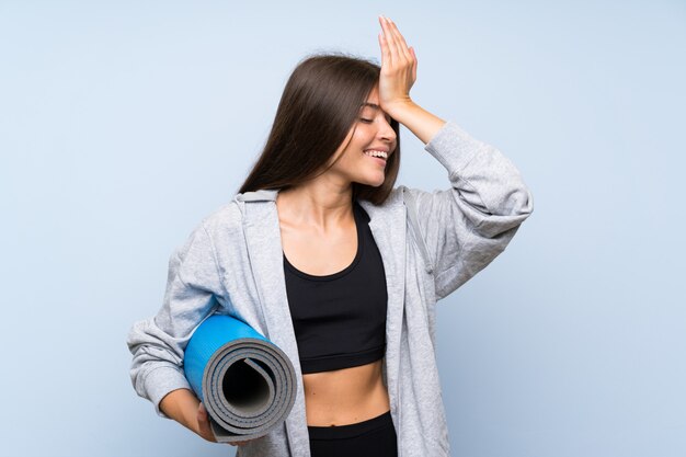 Jeune fille sportive avec tapis sur un mur bleu isolé a réalisé quelque chose et avait l'intention de la solution