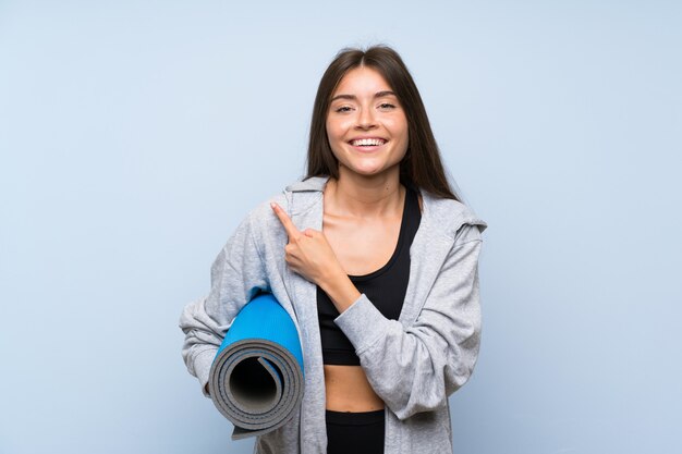 Jeune fille sportive avec tapis pointant sur le côté pour présenter un produit