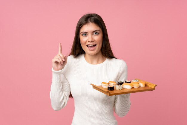 Jeune fille avec sushi sur fond rose isolé pointant vers le haut une excellente idée
