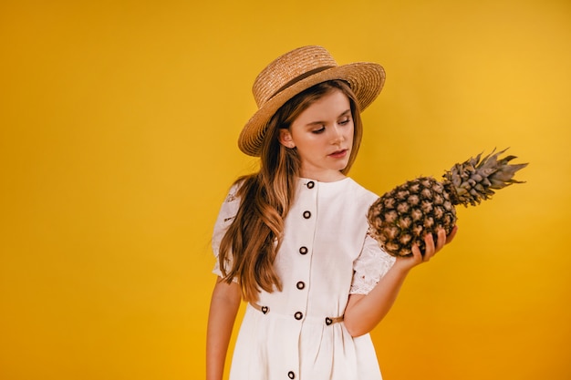 Jeune fille tenant un ananas mûr et gros sur fond jaune