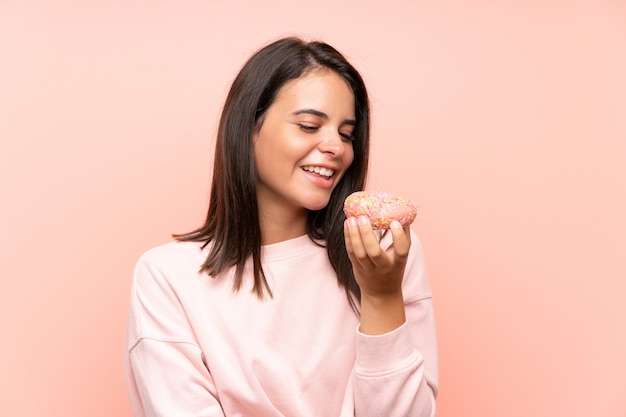 Jeune fille tenant un beignet sur un mur rose isolé