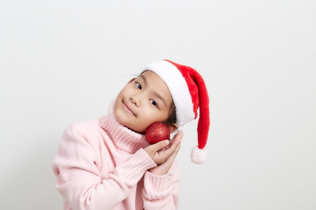 Jeune fille tenant une boule de Noël rouge en pull et bonnet de Noel