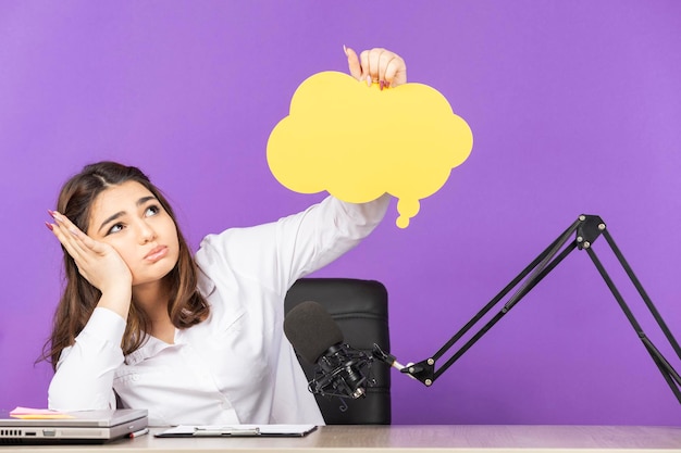 Jeune fille tenant une bulle de dialogue en papier et se sentant bouleversée alors qu'elle était assise sur le bureau Photo de haute qualité