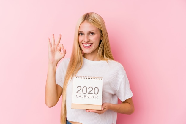 Jeune fille tenant un calendrier 2020 gai et confiant montrant un geste correct.