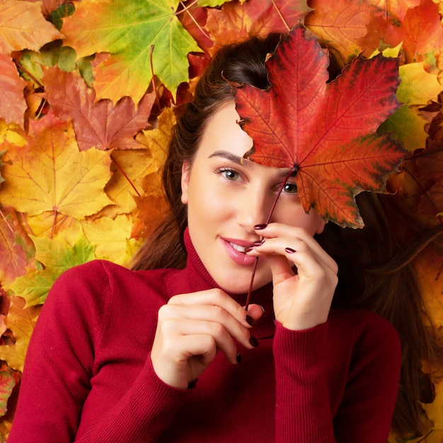 Jeune fille tenant une feuille d'érable rouge à la main sur fond coloré de feuilles mortes.