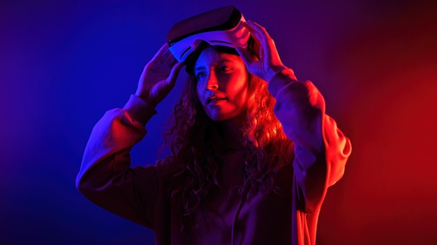 Jeune fille tenant des lunettes de réalité virtuelle sur sa tête avec un éclairage bleu et rouge dans la pièce. Divertissement à la maison